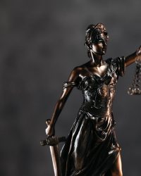 Description Detailed bronze Lady Justice statue with scales and sword against a dark background, symbolizing law and justice.