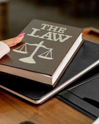 Description Closeup image of a law book titled 'The Law' on a wooden desk with scales of justice.